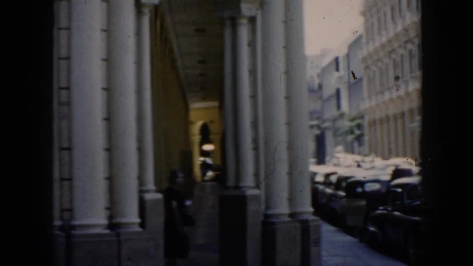 1956 Cuba street-level view of a colonnaded Havana walkway, parked cars, and a woman passing near the columns.