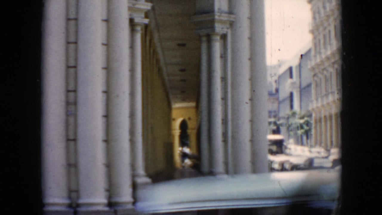 1956 Cuba 8mm frame showing a shaded arched colonnade with white pillars and a bright street view beyond.