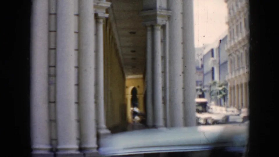1956 Cuba 8mm frame showing a shaded arched colonnade with white pillars and a bright street view beyond.