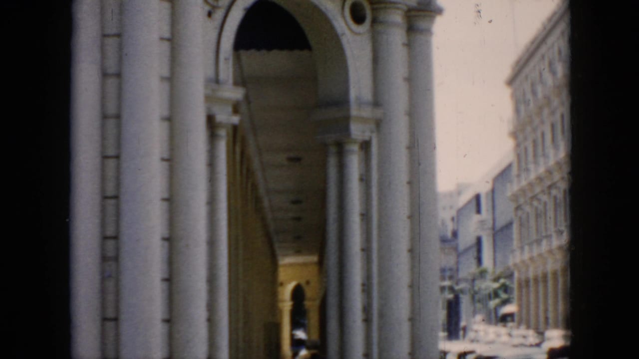 White columns and arched facade beside a bright street with distant buildings and cars.