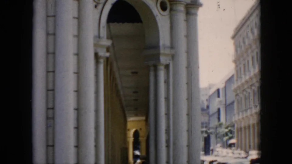 1956 Cuba street view framed by pale columns and a rounded arch, with traffic and facades visible in the distance.
