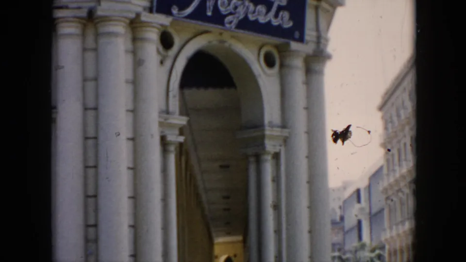 1956 Cuba 8mm frame showing an arched colonnade beneath a blue cursive sign, with the street partly visible beyond.