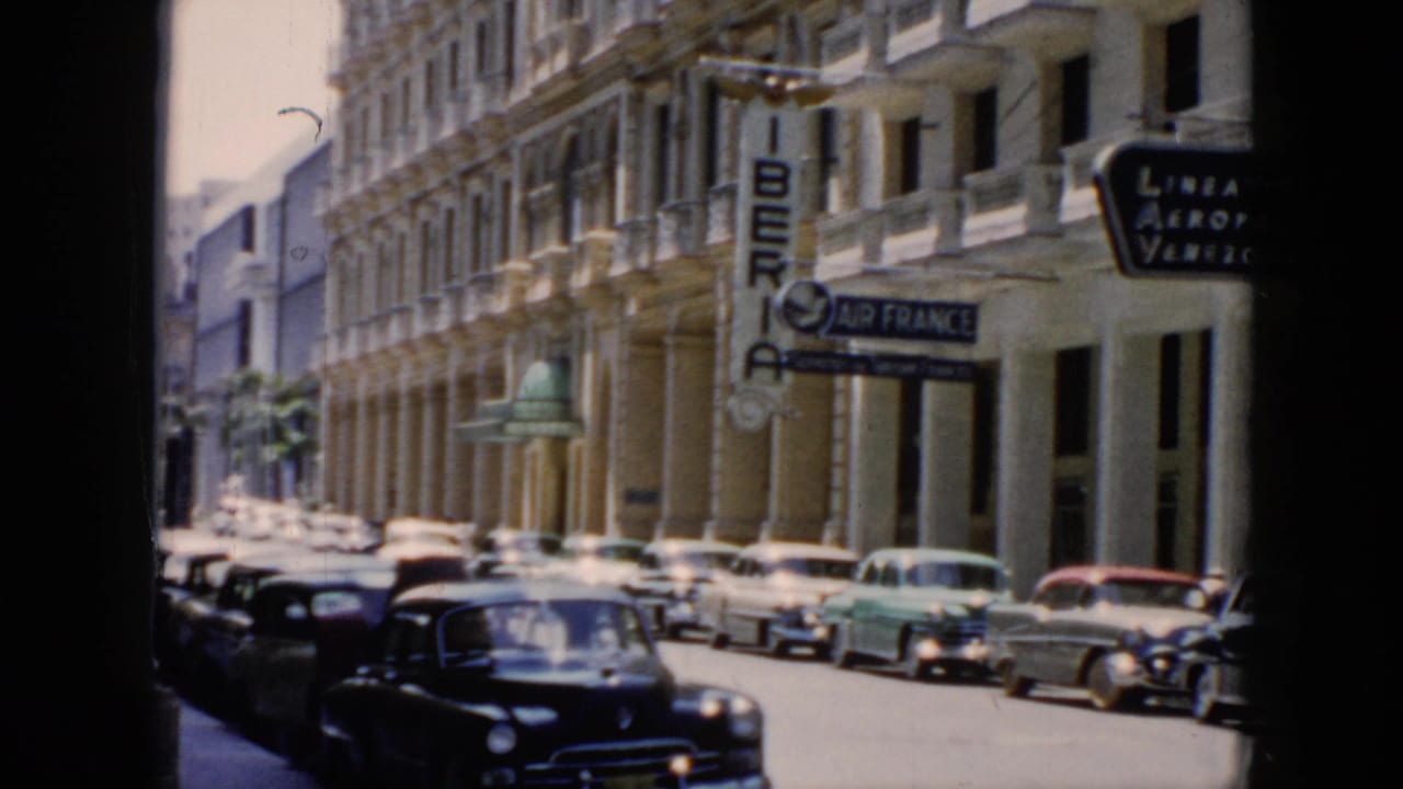 Sunlit urban street with parked classic cars, balconies, and Iberia and Air France signs.