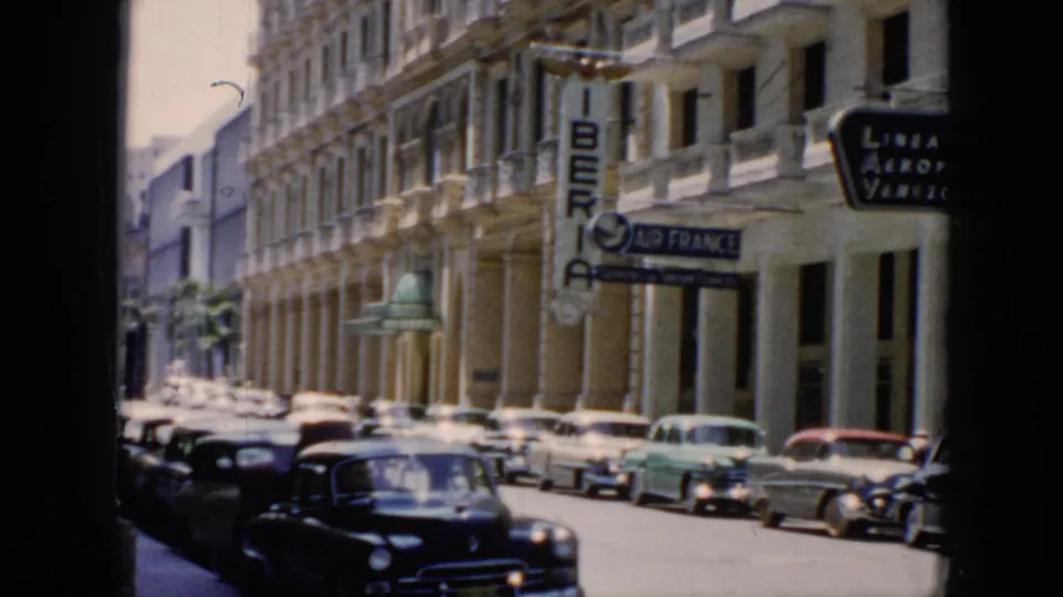 1956 Cuba street view with mid-century cars, ornate building balconies, and visible Iberia and Air France signage near the curb.
