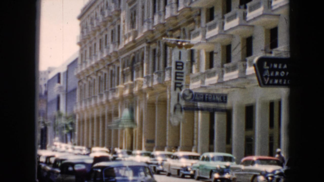 Street lined with parked cars beside a tall building with airline signage and balconies.