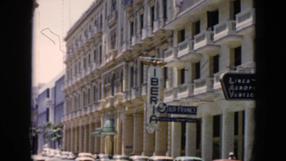 1956 Cuba home-movie frame of an urban street with classic cars, Iberia and Air France signs, balconies, and visible film wear.