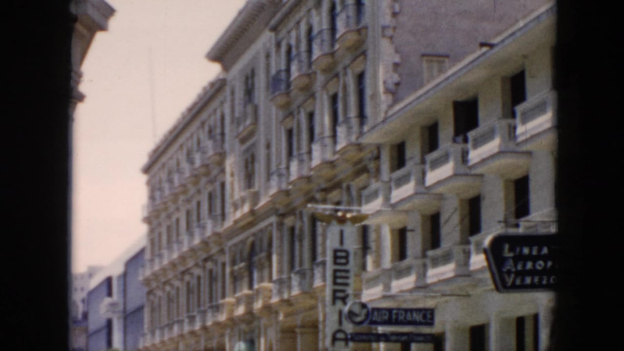 1956 Cuba street view from a dark archway showing ornate facades, balconies, and Iberia and Air France signs.