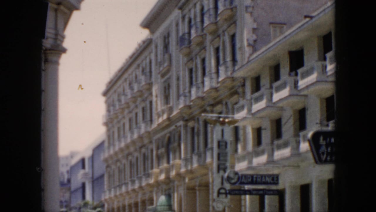 Balcony-lined street facade with visible airline signs under a shaded edge.