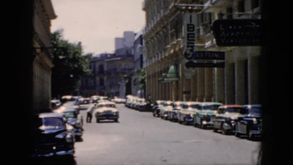 1956 Cuba street looking down a car-lined block with distant people and Iberia and Air France signs near the foreground.