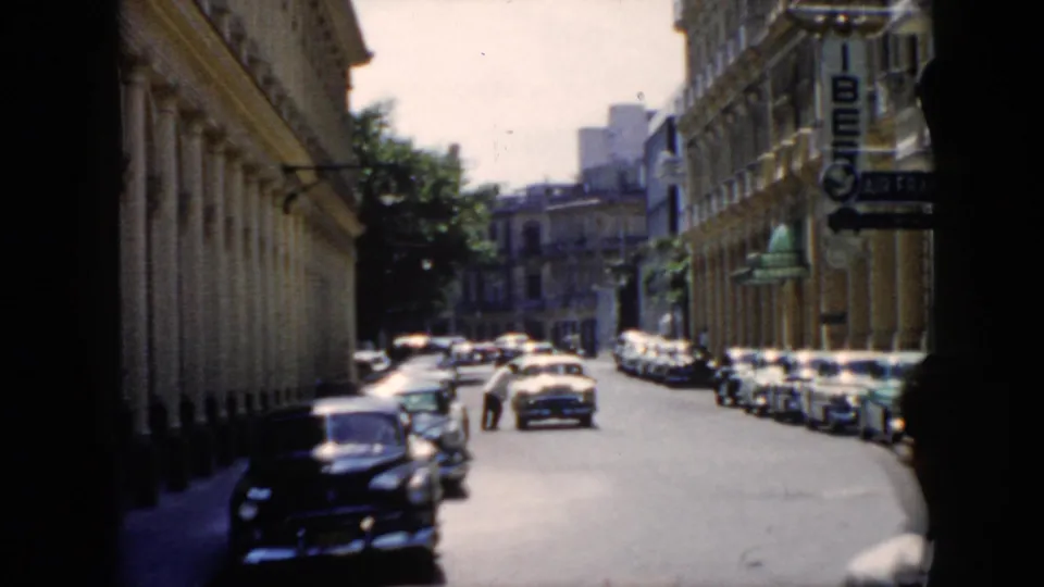 1956 Cuba urban street with parked mid-century automobiles, a stopped car, pedestrians, and Air France signage.