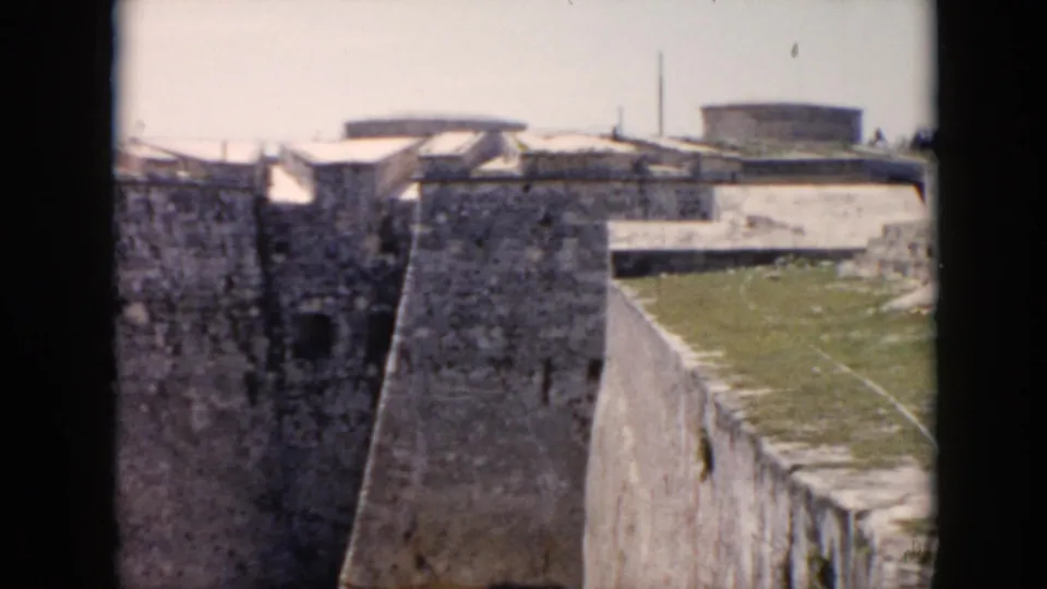 A cutaway shows a weathered stone fortification or wall in Cuba, with rough masonry, a grassy upper area, and sunlit exterior surfaces.