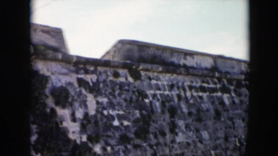 The final 1956 Cuba frame shows the fortress wall from below, with weathered stonework, a raised upper section, and dark foreground edges.