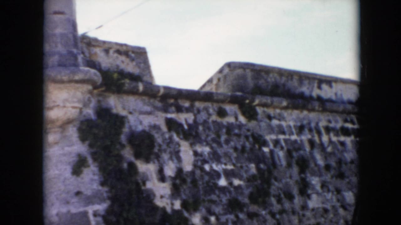 1956 Cuba 8mm frame showing a close view of a weathered stone fortress wall with moss-darkened masonry and a partial turret.