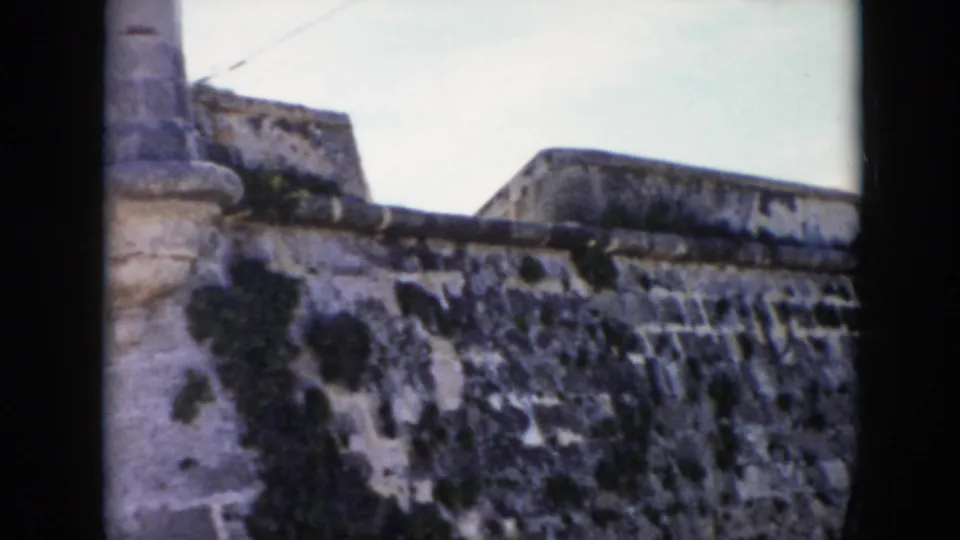 1956 Cuba 8mm frame showing a close view of a weathered stone fortress wall with moss-darkened masonry and a partial turret.