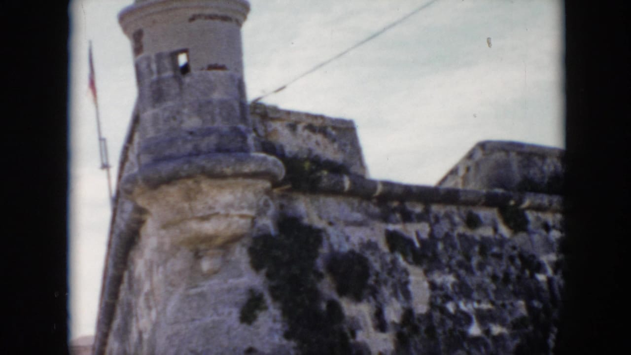 1956 Cuba 8mm frame with a cylindrical stone turret, fortress wall, flagpole, and pale overcast sky.