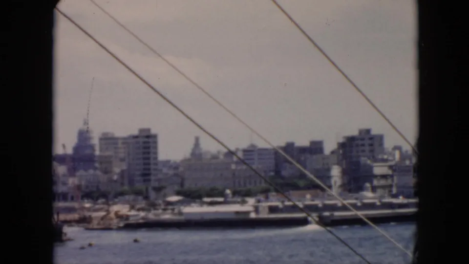 1956 Cuba frame showing a harbor skyline through window framing, with water, a moored vessel, buildings, and diagonal wires.