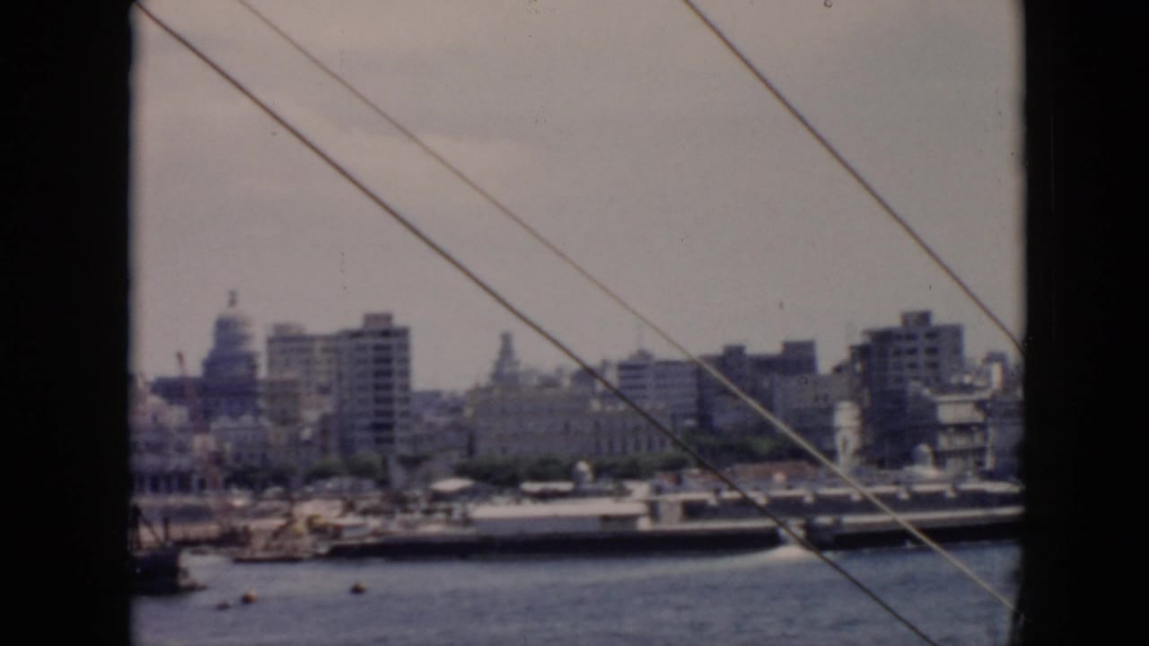 1956 Cuba harbor view from a vessel, showing waterfront buildings, domes, moored ships, and diagonal ship rigging.