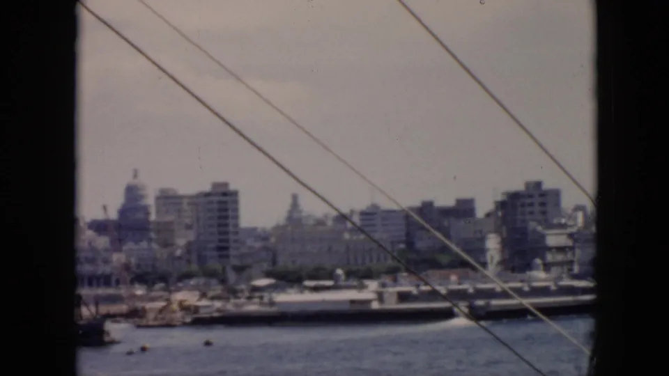 1956 Cuba harbor view from a vessel, showing waterfront buildings, domes, moored ships, and diagonal ship rigging.