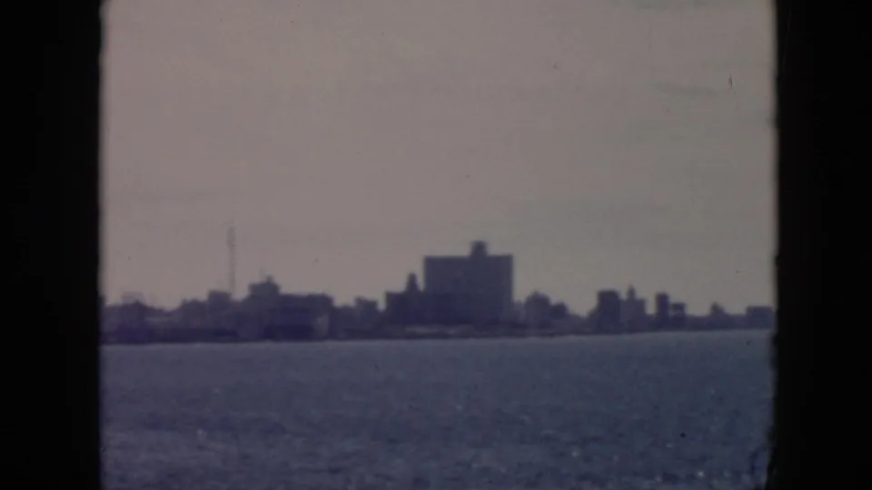 1956 Cuba harbor shoreline with a low urban silhouette, a thin vertical mast or tower, and calm water in the foreground.