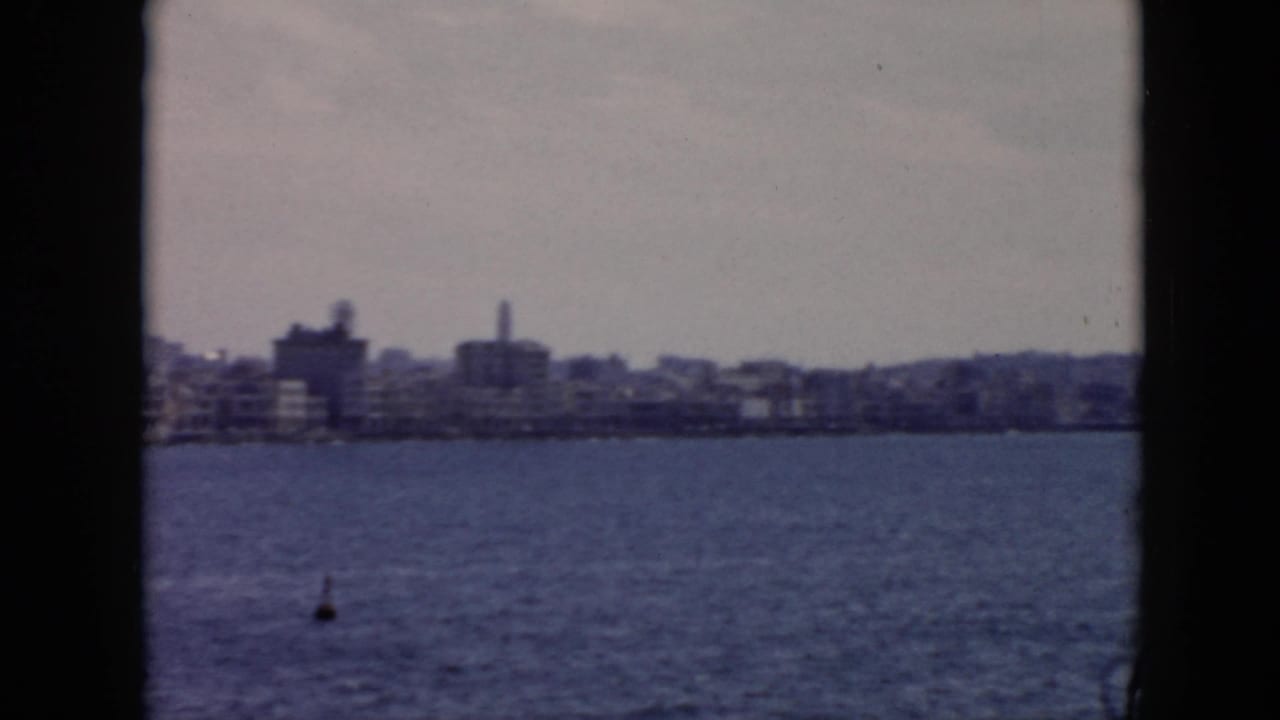 1956 Cuba home-movie view of a waterfront skyline across open water, framed by dark vessel or film edges.