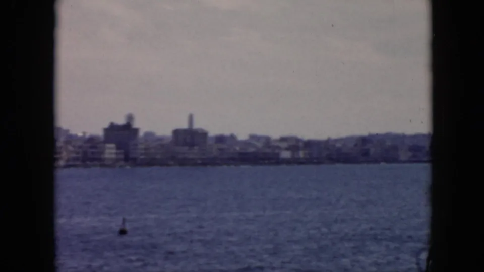 1956 Cuba home-movie view of a waterfront skyline across open water, framed by dark vessel or film edges.