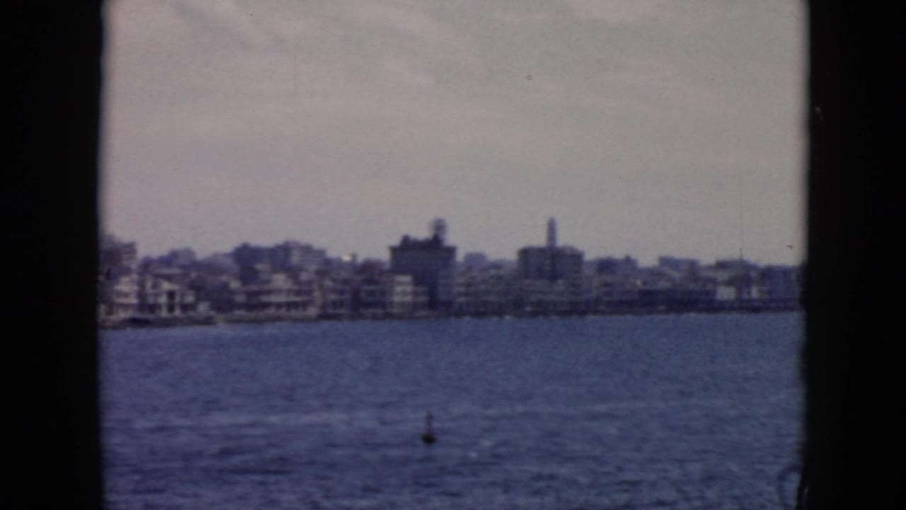 A 1956 Cuba waterfront panorama continues across calm water, with low buildings and muted 8mm color.