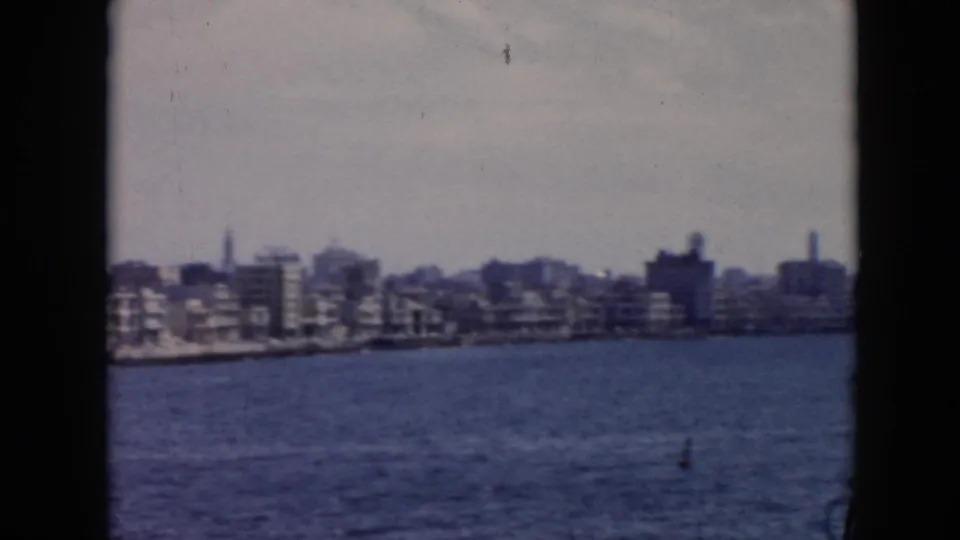 1956 Cuba coastal city frontage seen from a moving vessel, with water foreground and softened mid-century building shapes.