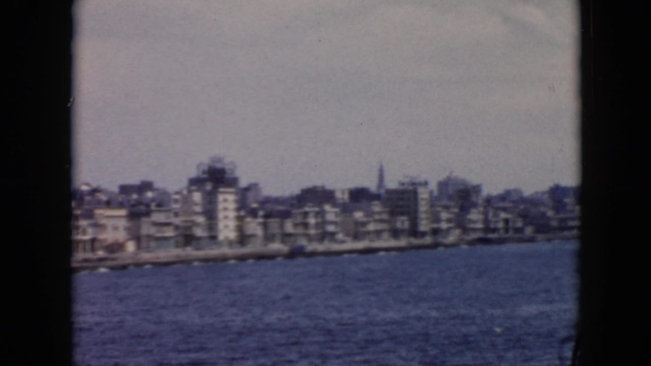 Coastal city skyline across choppy water, framed by dark 8mm film borders.