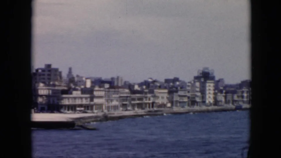 1956 Cuba waterfront with a pier or dock, small boats, multi-story buildings, and rough water in the foreground.