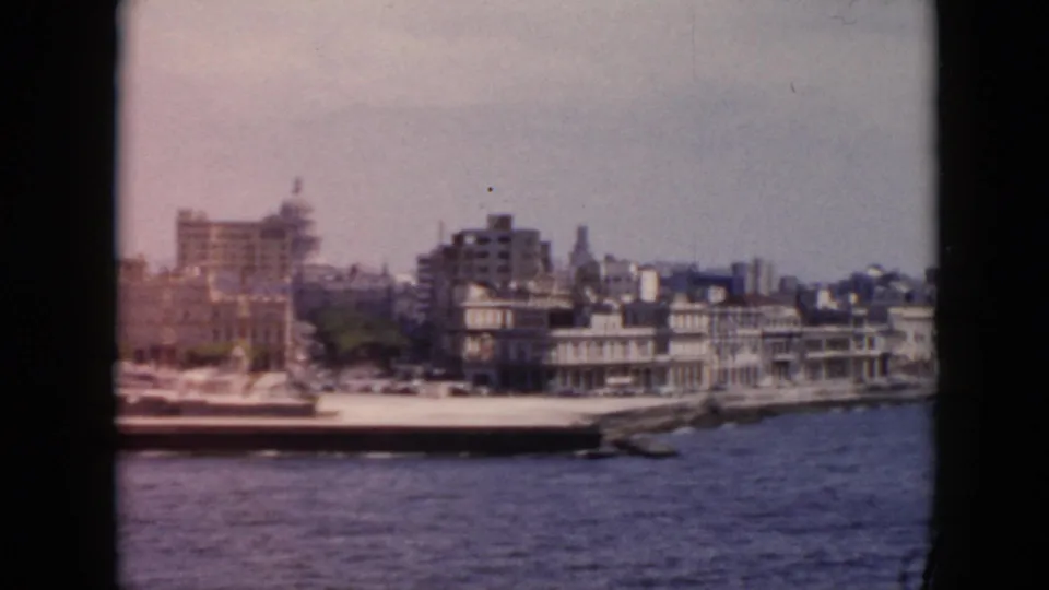 1956 Cuba waterfront view from a moving boat, with low-rise shoreline buildings, taller blocks, and harbor water in front.