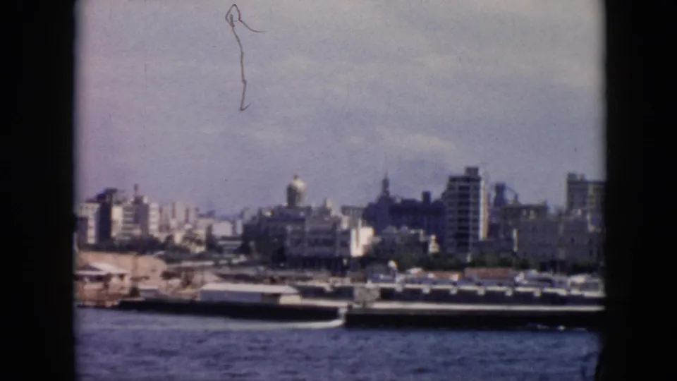 1956 Cuba harbor view with moored boats, waterfront construction or open shoreline, high-rises, and a prominent dome visible inland.