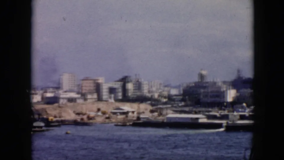 1956 Cuba waterfront panorama from the harbor, showing boats, a quay, mixed urban buildings, and a dome softened by 8mm grain.