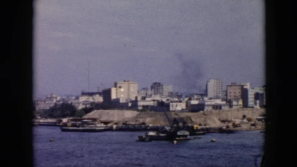 1956 Cuba harbor view from a vessel, with small boats on calm water and low to mid-rise buildings along the shore.
