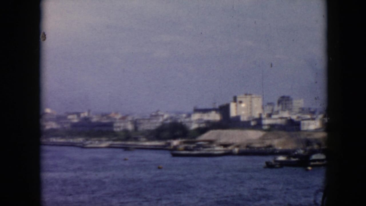 Cuban coastal city waterfront in 1956, seen across the harbor with boats near the shore and soft, grainy 8mm framing.