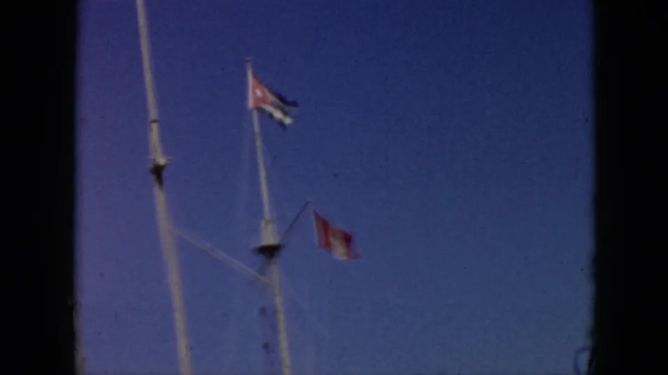 1956 Cuba home-movie frame showing a Cuban flag and another red-and-white flag flying from boat rigging against blue sky.