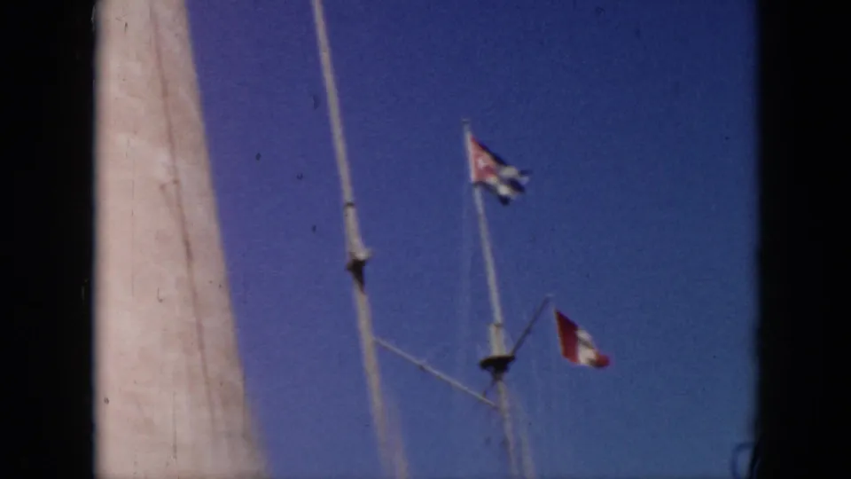 1956 Cuba frame focused on a Cuban flag, a red-and-white flag, mast rigging, and a tall white structure against clear sky.