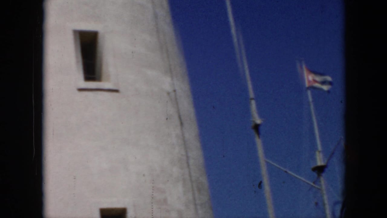 1956 Cuba 8mm frame showing a tall white lighthouse facade, narrow windows, blue sky, flagpole, and small Cuban flag.