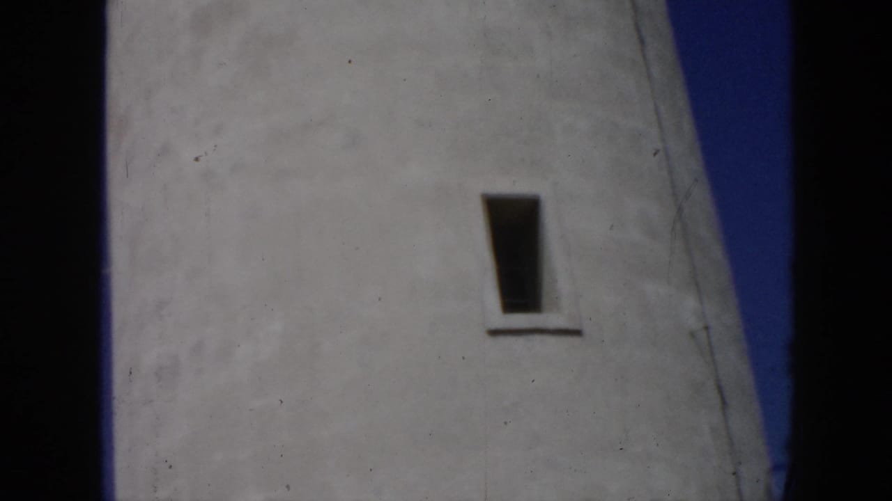 1956 Cuba 8mm frame of the lighthouse facade, centered on a single narrow window and pale weathered masonry.