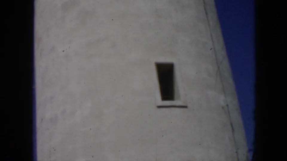 1956 Cuba 8mm frame of the lighthouse facade, centered on a single narrow window and pale weathered masonry.