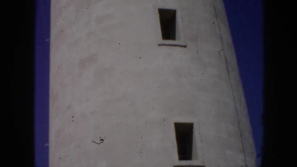 1956 Cuba 8mm frame looking upward along a weathered white lighthouse wall with two narrow rectangular windows.