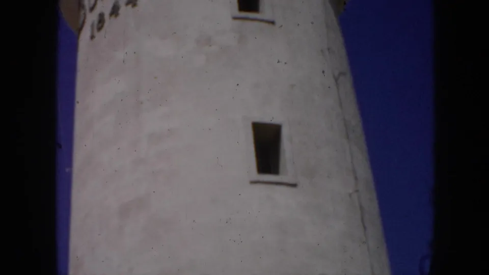 1956 Cuba 8mm frame showing the upper white lighthouse facade with narrow windows and blue sky along the side.