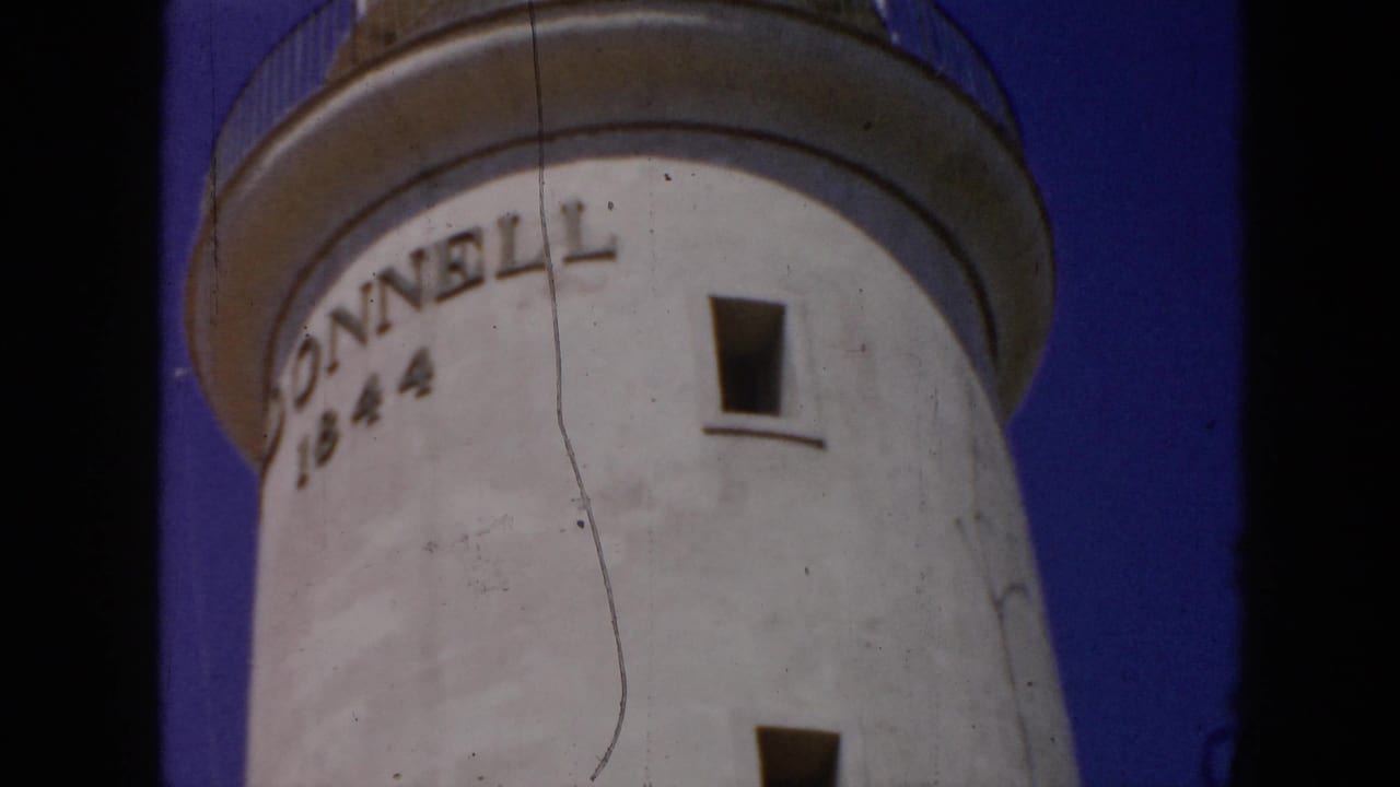 1956 Cuba 8mm frame showing the lighthouse tower side with DONNELL 1844 lettering, a small window, and clear blue sky.