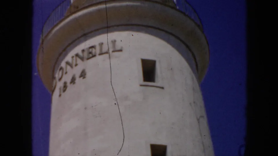 1956 Cuba 8mm frame showing the lighthouse tower side with DONNELL 1844 lettering, a small window, and clear blue sky.
