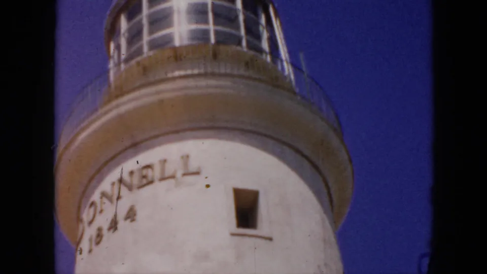 1956 Cuba 8mm frame showing a closer low-angle view of the lighthouse tower, visible inscription, small window, and lantern room.