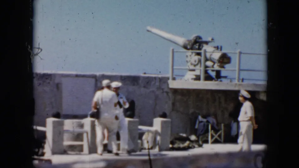 1956 Cuba 8mm frame with sailors in white uniforms standing below a mounted cannon on a concrete military platform.