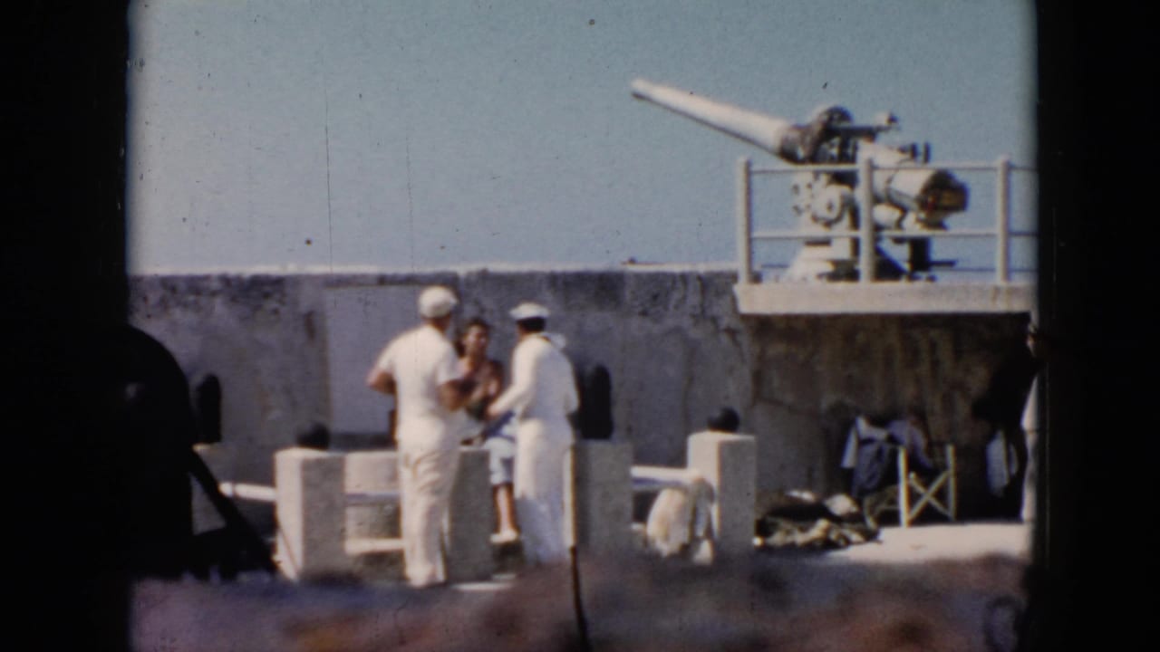 1956 Cuba footage shows two sailors and a civilian visitor on a warship deck, with a large mounted gun above them.