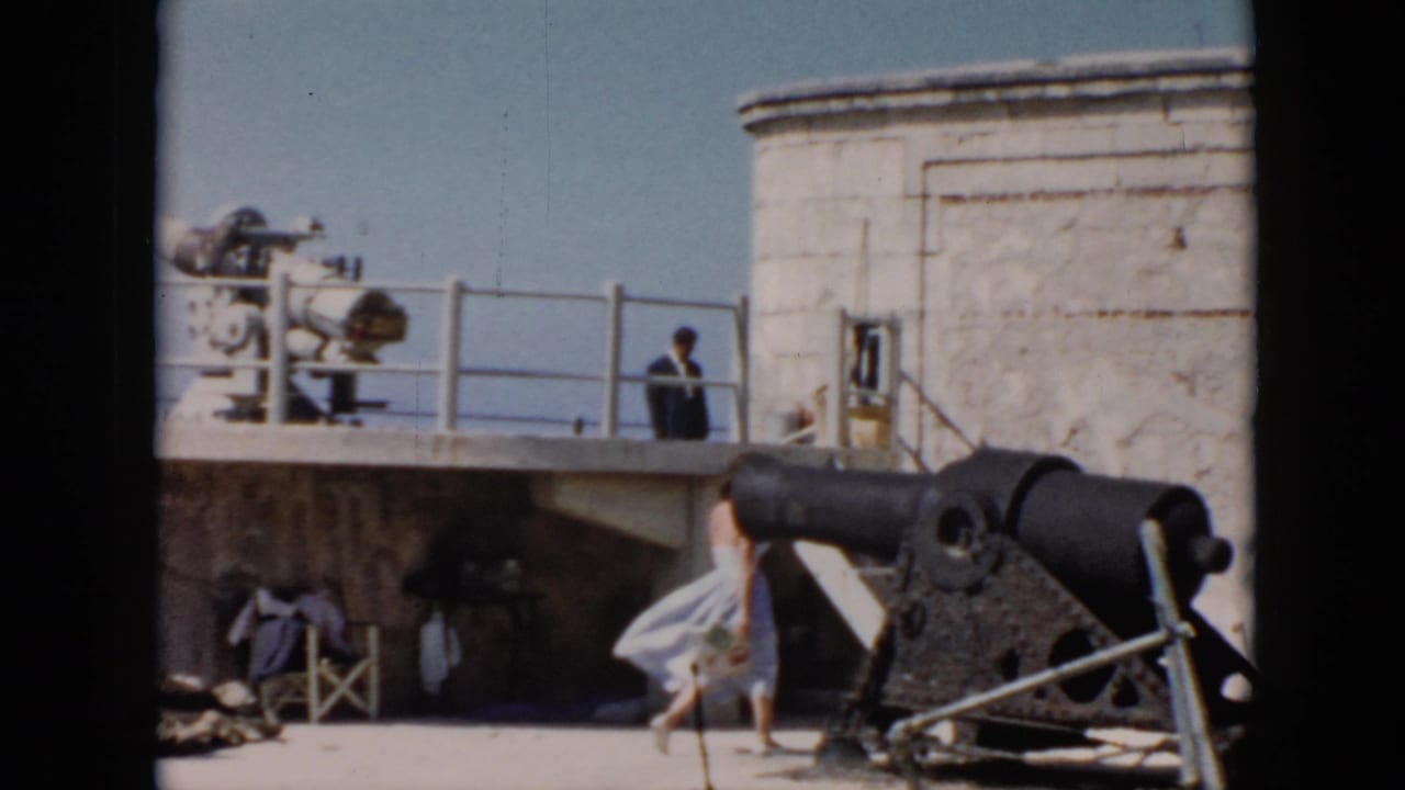 Woman in a light dress passes the cannon in a fort courtyard.