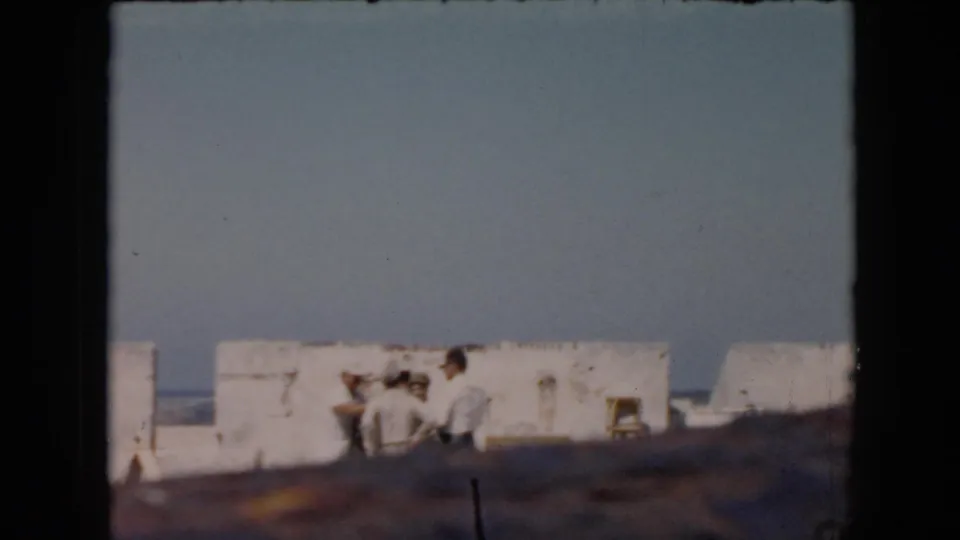 1956 Cuba frame showing a small group beside whitewashed fort walls, with blue sky, a possible sea horizon, and soft 8mm framing.