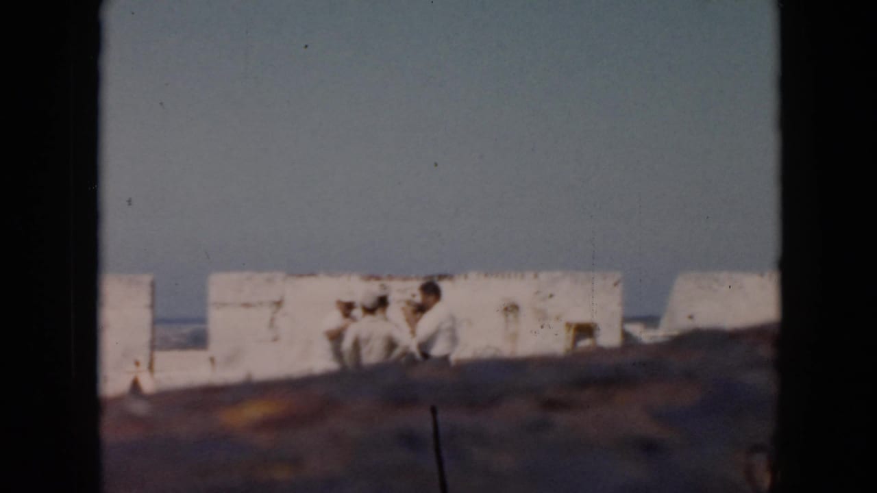 1956 Cuba home-movie frame showing tourists beside weathered white fortress walls with sea and sky beyond.