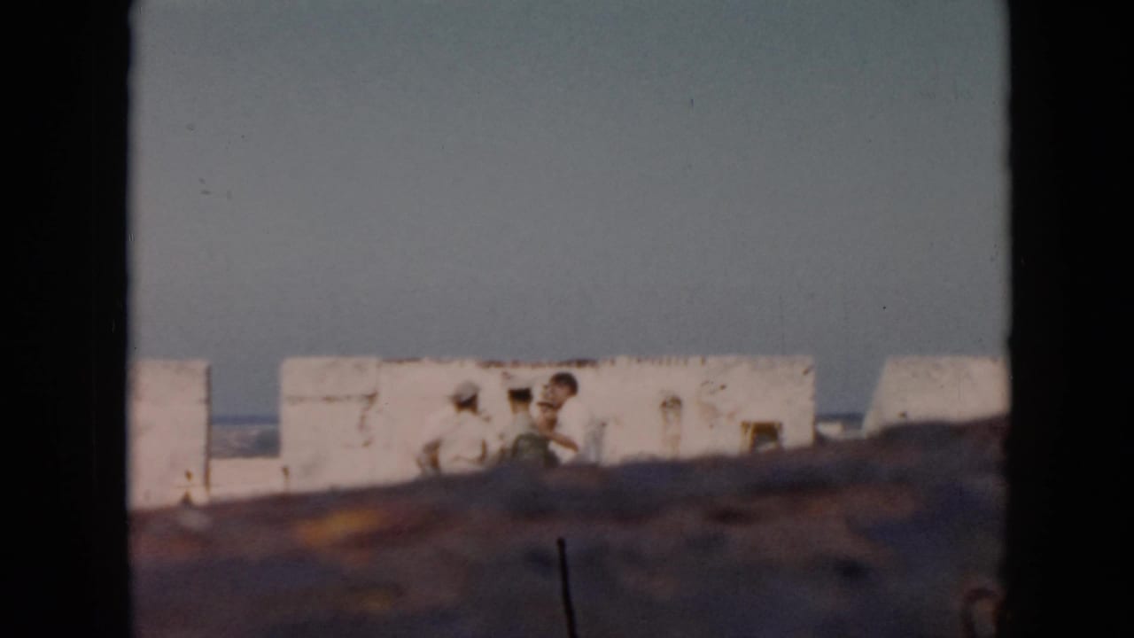 Several people stand by white stone walls with sea in the background.